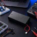 Black 18650 battery holder with red/black wired leads on a workbench with jumper wires and test equipment.