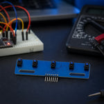 5-channel IR line-tracking sensor board on an electronics workbench beside a breadboard, multimeter, and jumper wires.