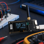 LILYGO TTGO LoRa32 ESP32 development board with OLED display and antenna on an electronics workbench with breadboard and multimeter