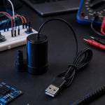 5V USB submersible mini water pump on an electronics workbench with a breadboard, multimeter, and test leads in the background
