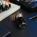 10K potentiometer with knob on an electronics workbench next to a breadboard and multimeter.