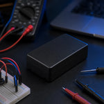 Black project enclosure box resting on a dark workbench near a breadboard and test leads.