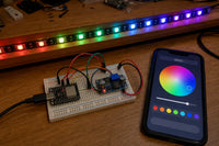 ESP32-C3 SuperMini and buck converter on a breadboard driving a glowing WS2812B RGB LED strip, controlled from a phone color-picker app