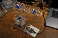 4-DOF acrylic robotic arm kit with SG90 servos, breadboard and ESP32-S3, mid-motion gripping an object