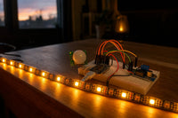 WS2812B LED strip glowing warm on a desk edge, wired to PIR sensor and ESP32-C3 on a breadboard