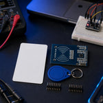 RC522 RFID reader module, white card, and blue keyfob with pin headers on an electronics workbench