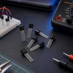 BC-series TO-92 transistor assortment on an electronics workbench with a breadboard, multimeter, and tweezers.
